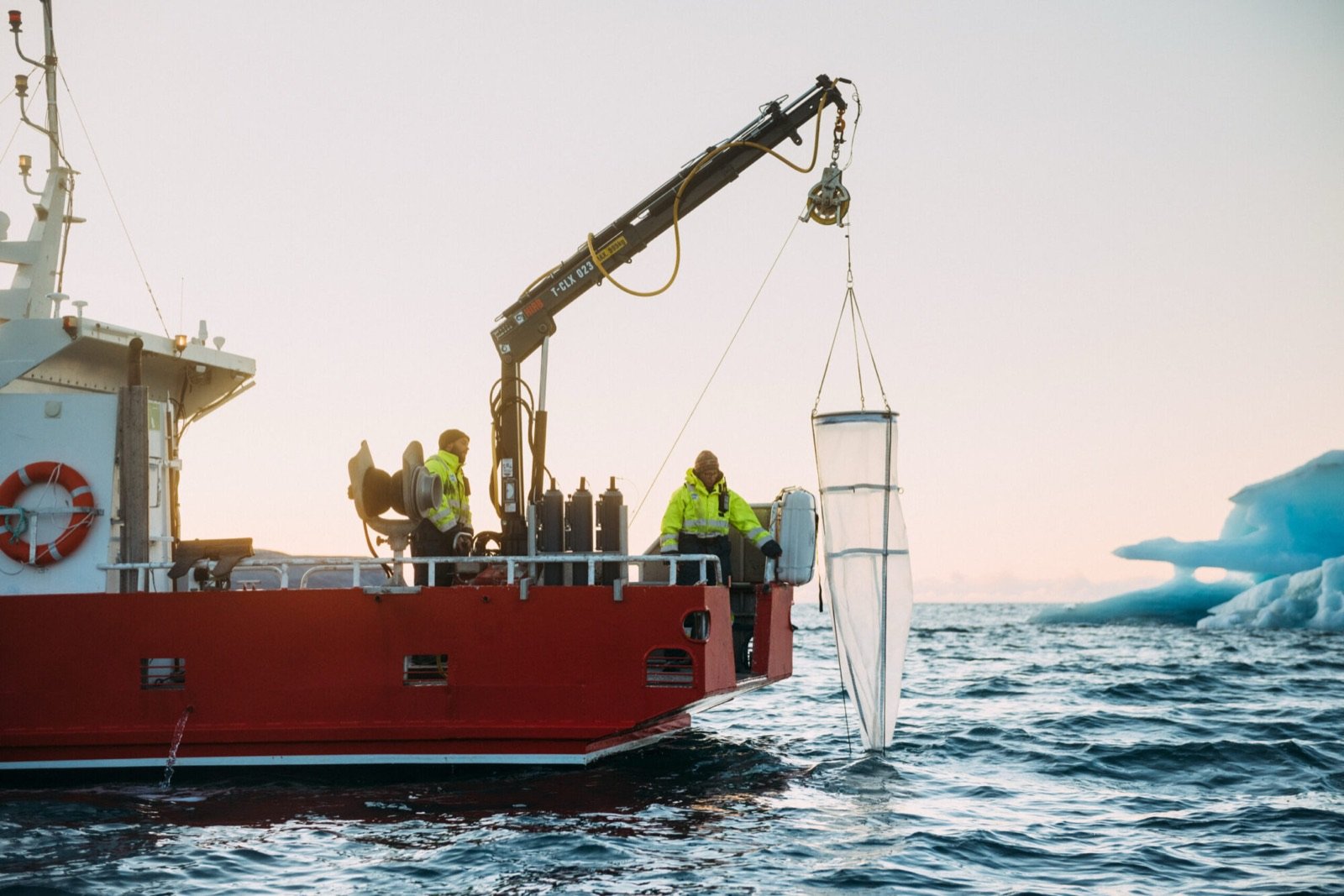 Researchers lowering a sampling net from a red boat in Kongsfjorden