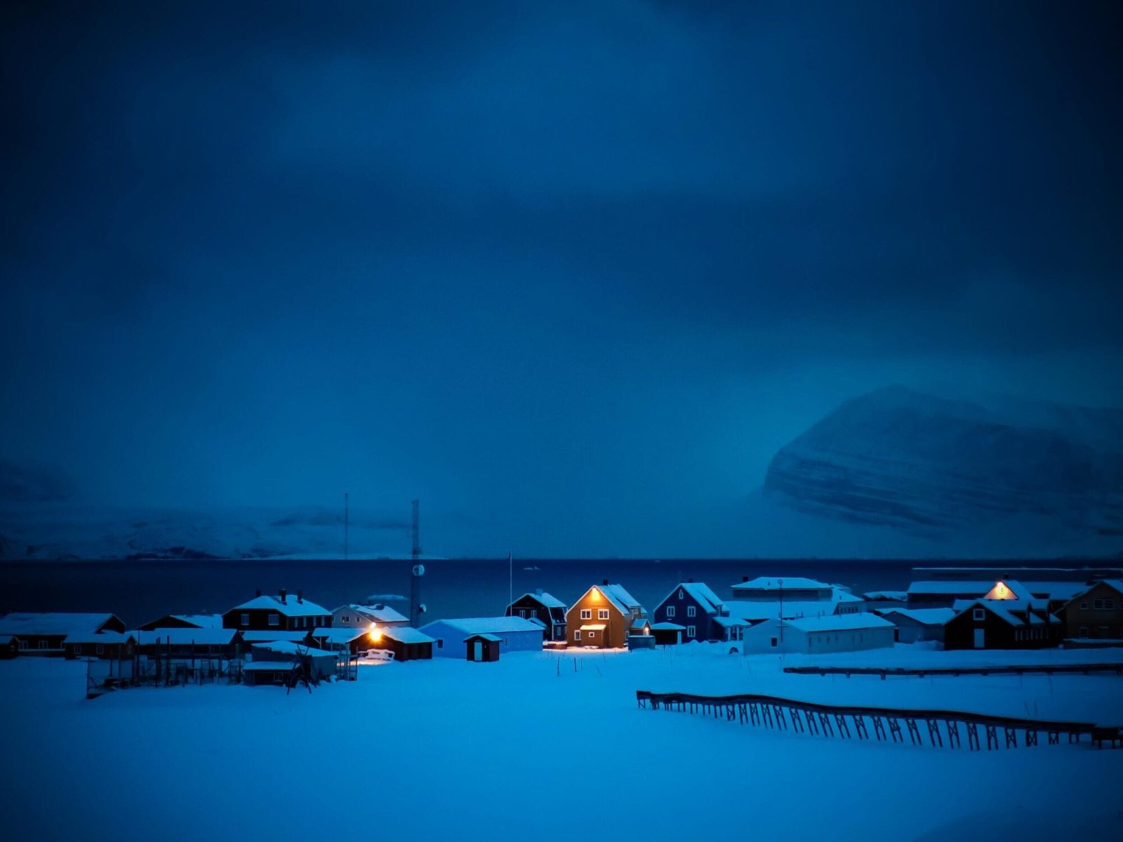 Ny-Ålesund under the blue light of the polar night, with lit windows along the shore